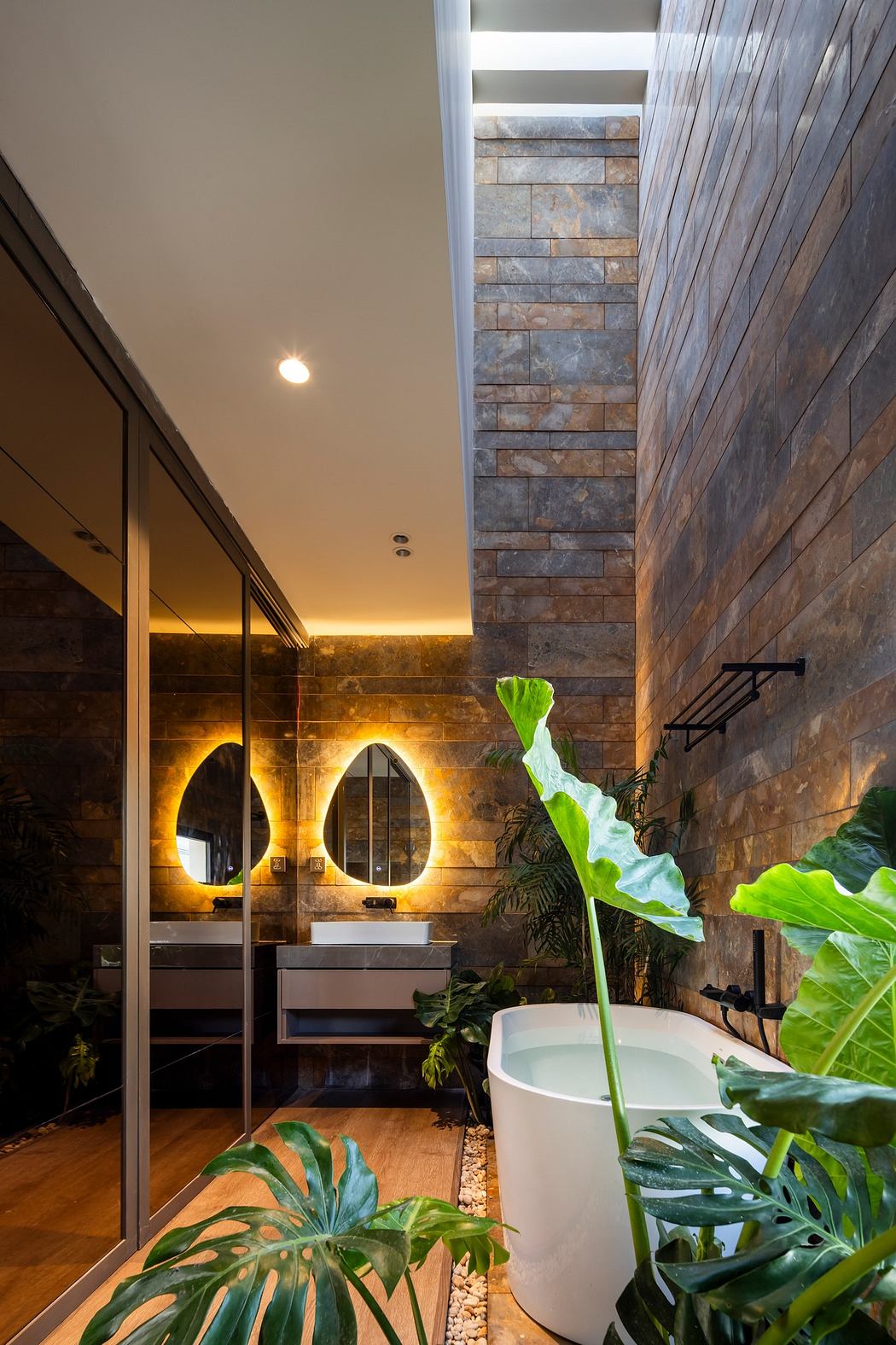 Modern bathroom with stone walls, green plants, and a freestanding tub.