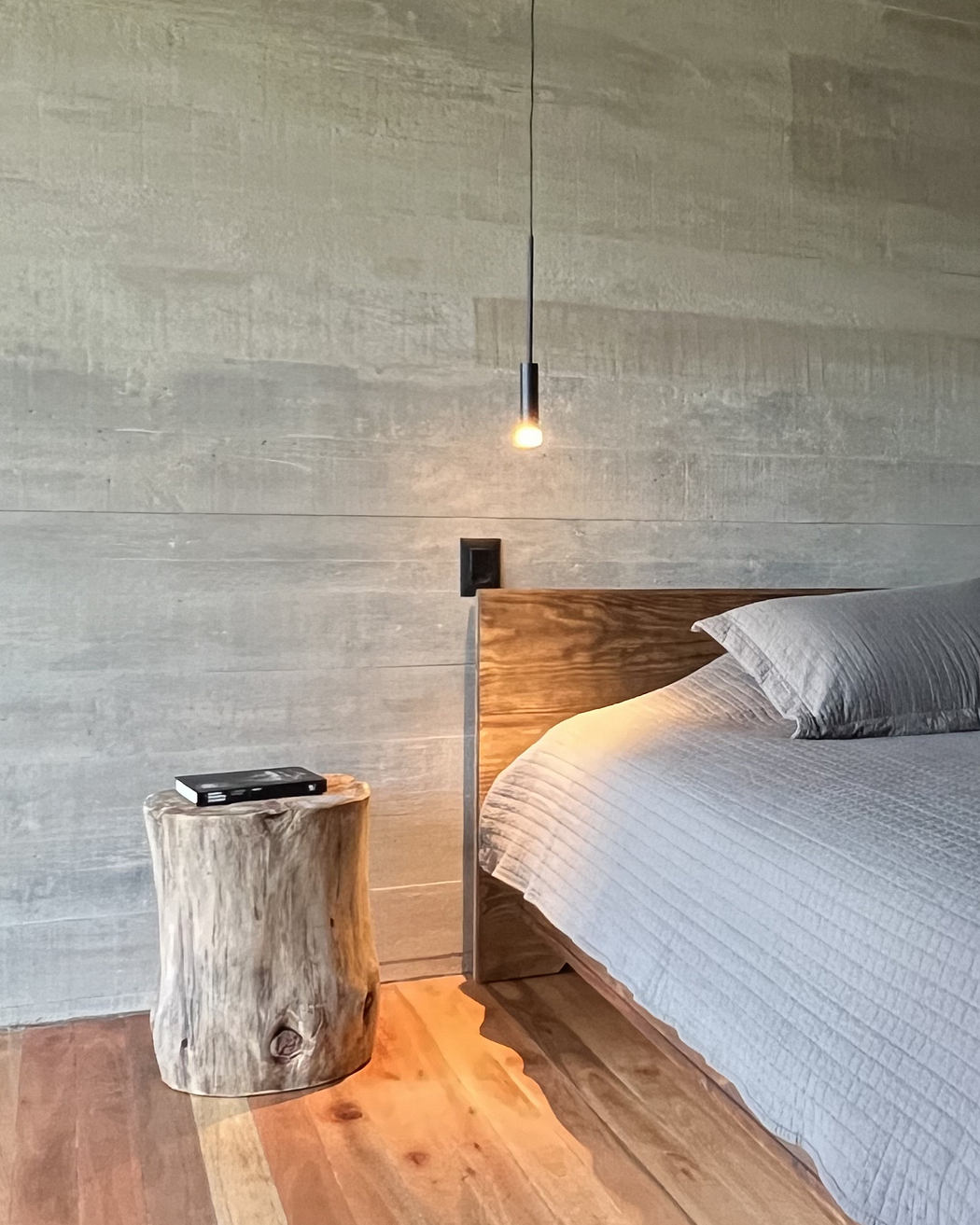 Modern bedroom with textured gray walls, pendant light, and natural wood bedside stump.