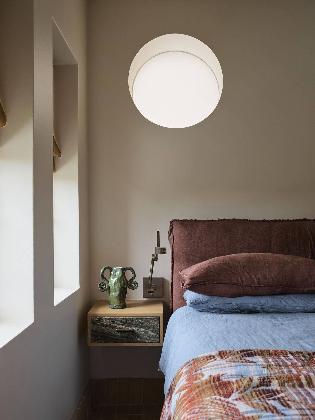Modern bedroom corner with circular wall lamp, bedside table, and earth-toned bedding