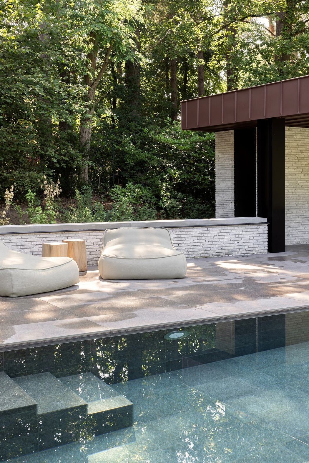 Modern outdoor poolside with stylish furniture and forest backdrop.