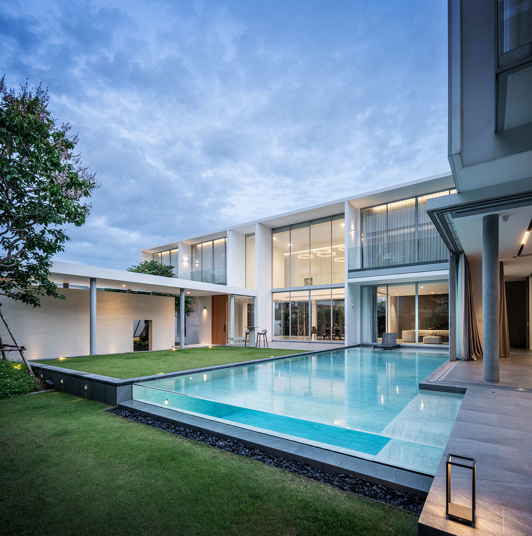 Modern two-story house with large windows and a pool at dusk.