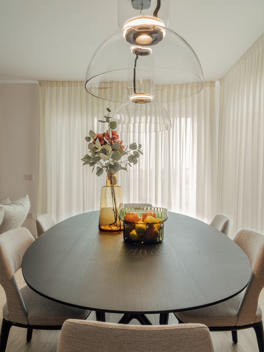 Modern dining area with a round table, pendant light, and sheer curtains.