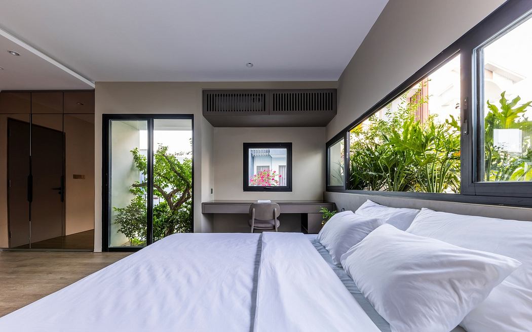 Modern bedroom with large windows, white bedding, and a view of greenery.