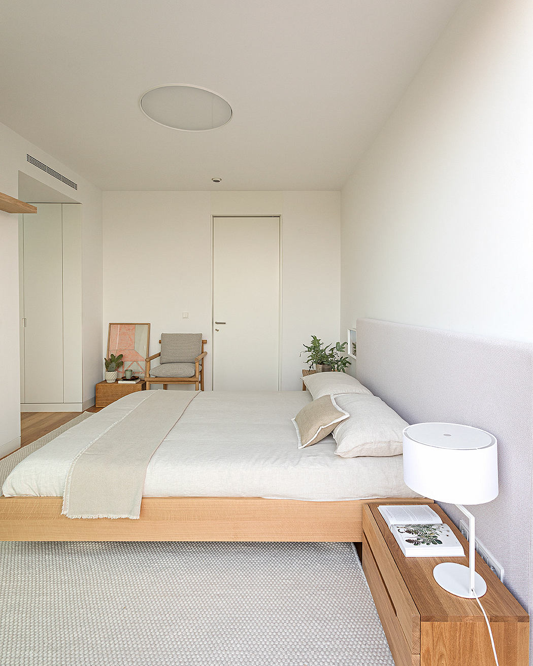 Minimalist bedroom with wooden bed, white bedding, and a modern lamp.