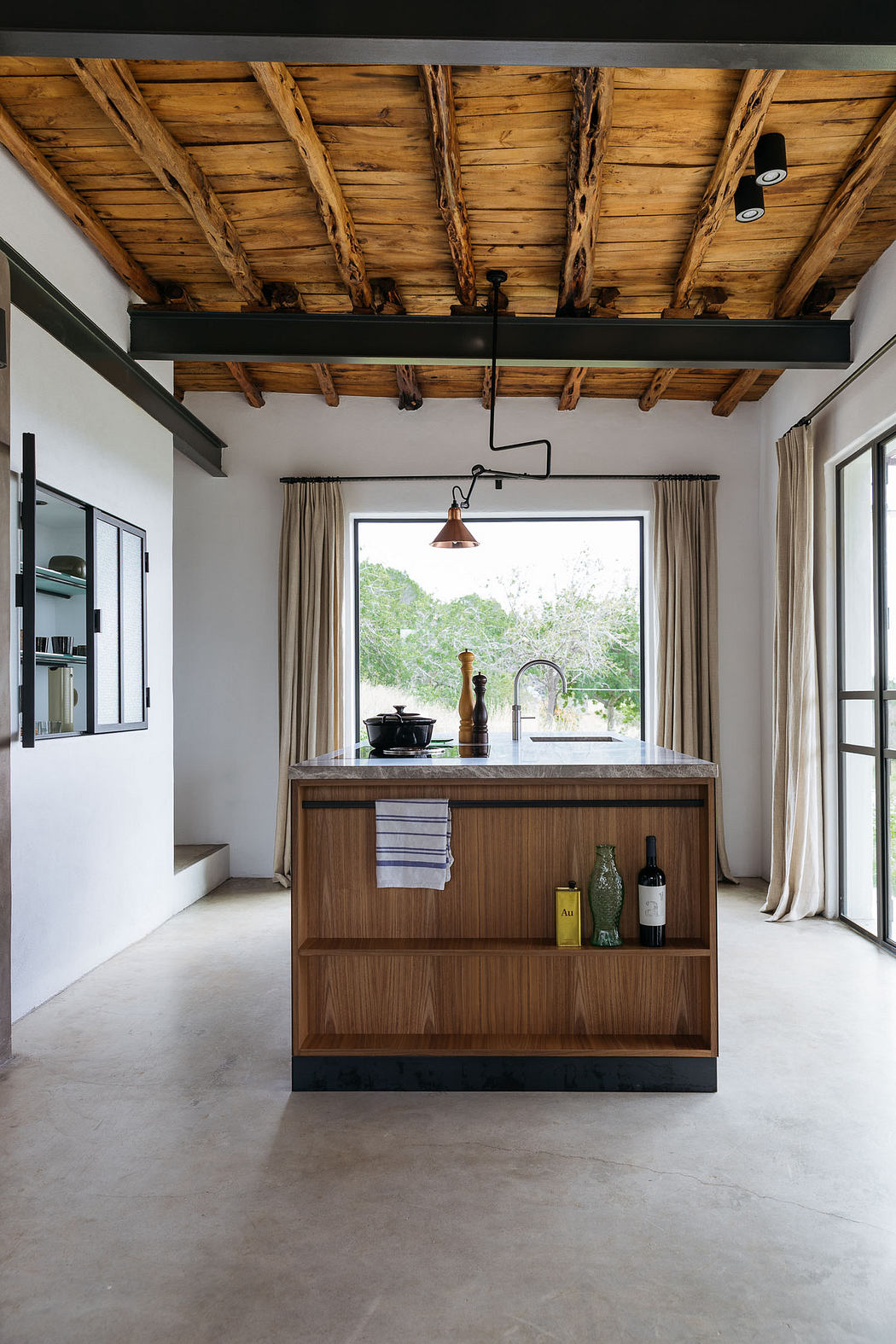 Modern kitchen interior with wooden island, rustic ceiling, and concrete floor.