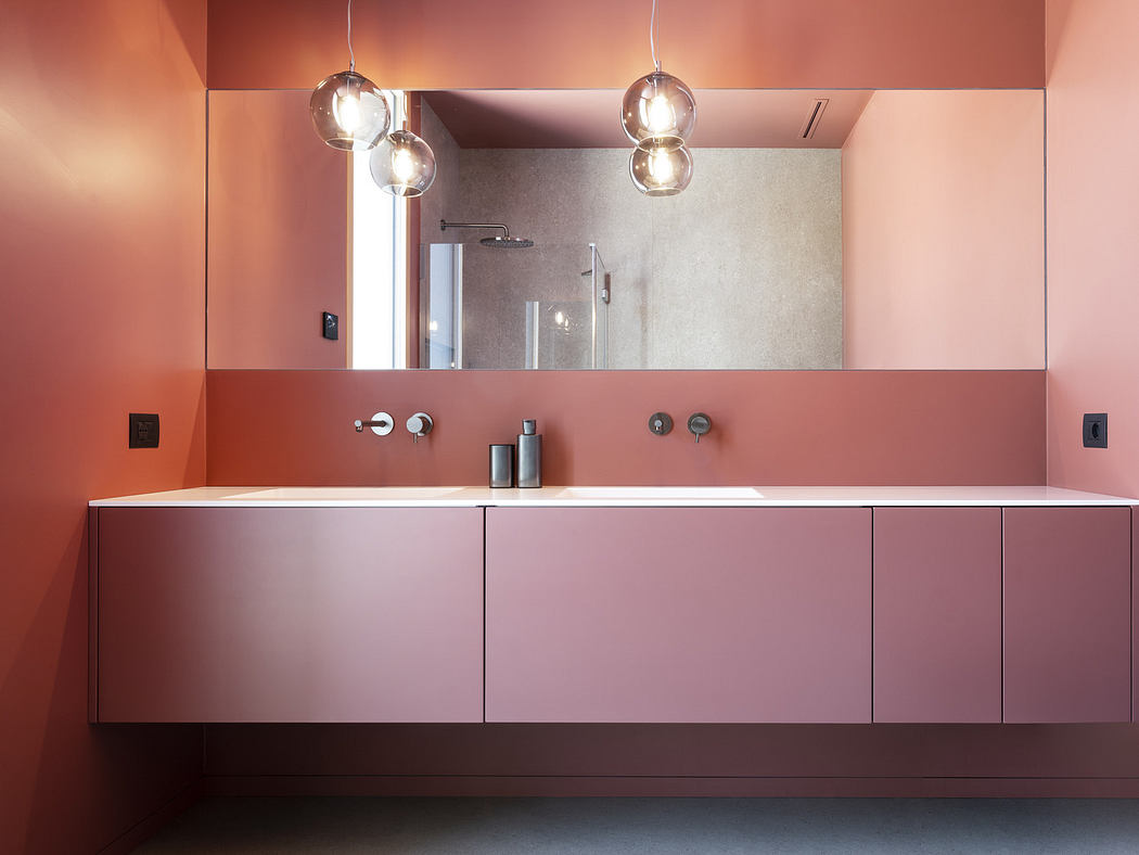Modern bathroom with pink cabinets, mirror, and pendant lights.
