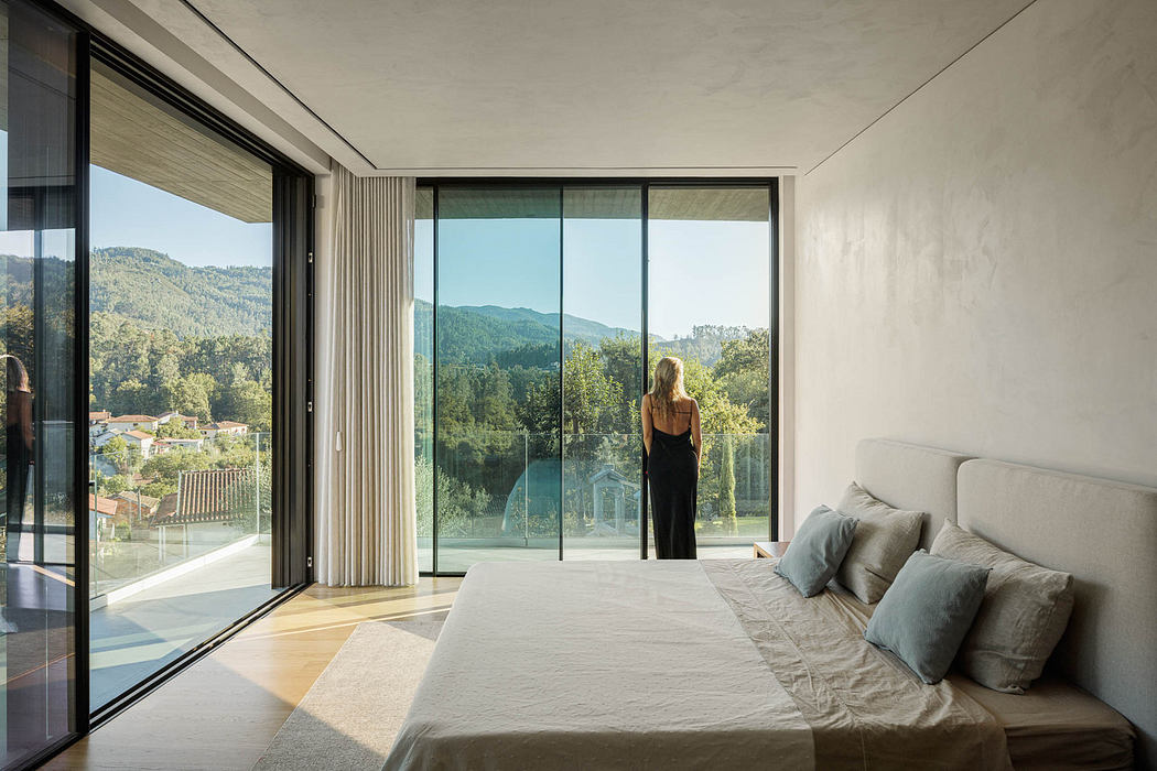 Modern bedroom with large windows overlooking nature, and a person standing by the view.