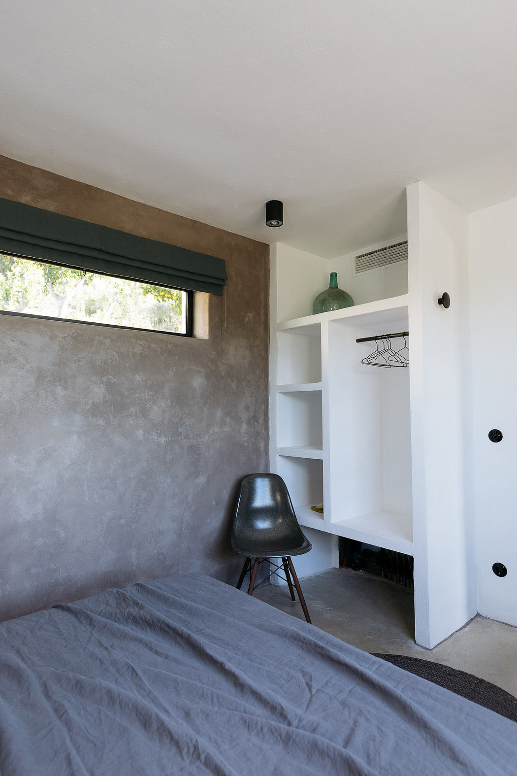 Modern minimalist bedroom with a concrete wall and built-in white shelving.