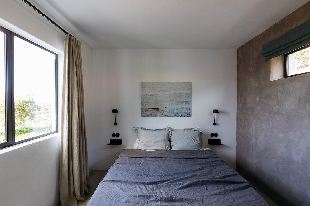 Minimalist bedroom with a concrete wall, white bedding, and ocean artwork.