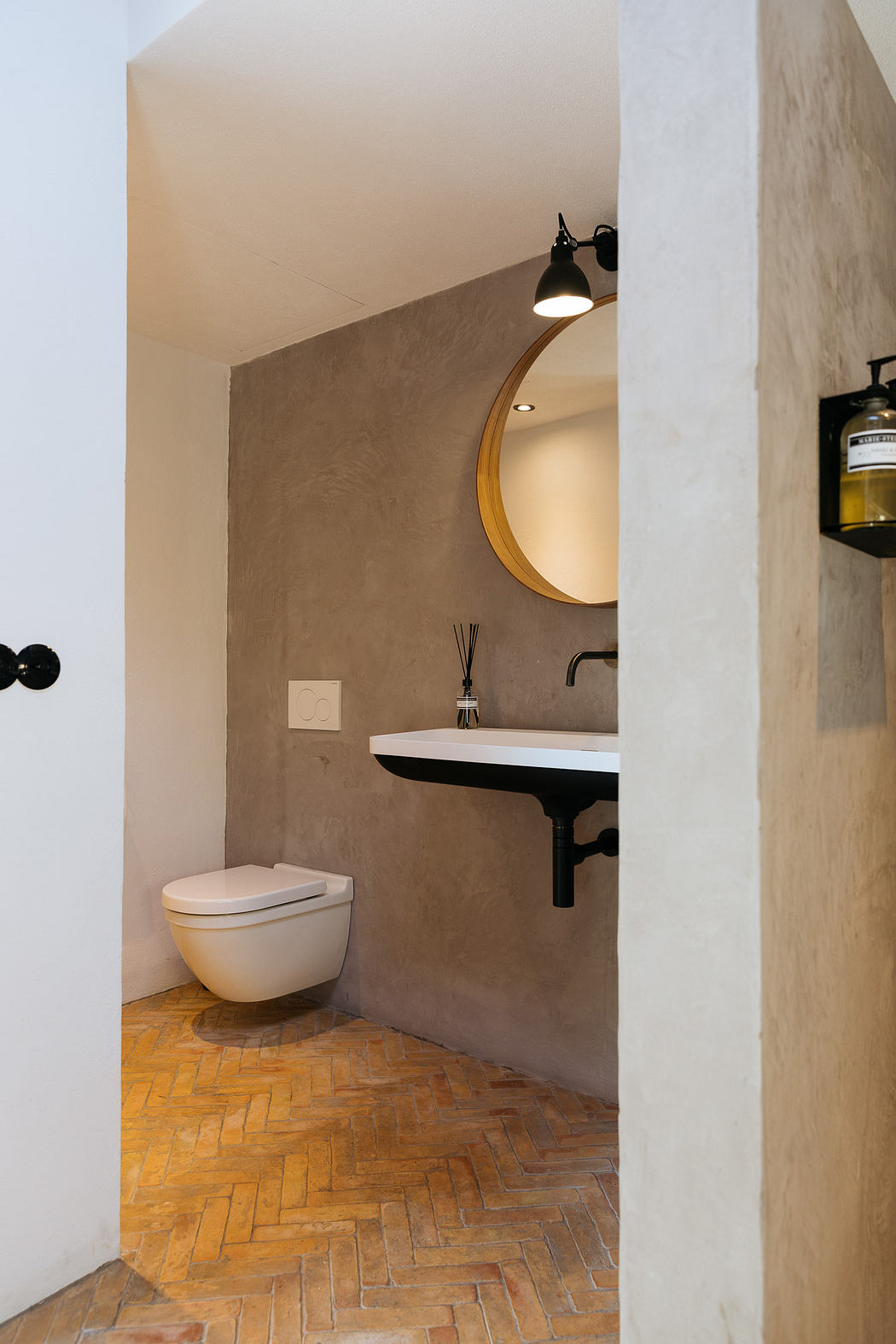 Modern bathroom with herringbone floor and round mirror.