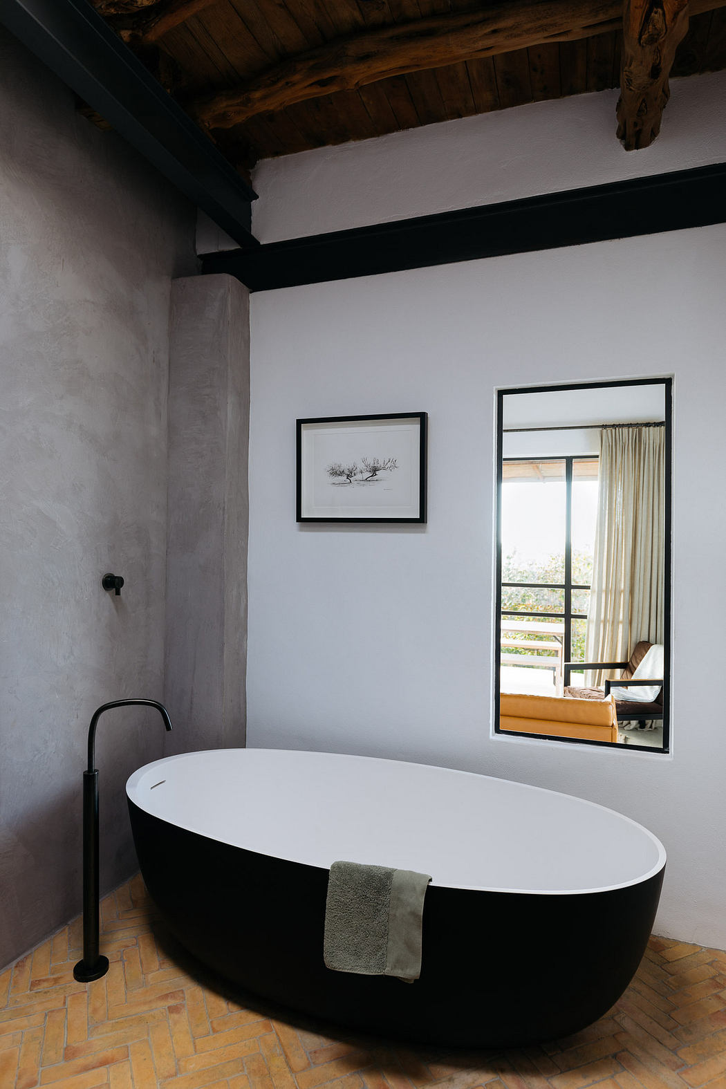 Modern bathroom with a standalone black and white tub, beamed ceiling, and a