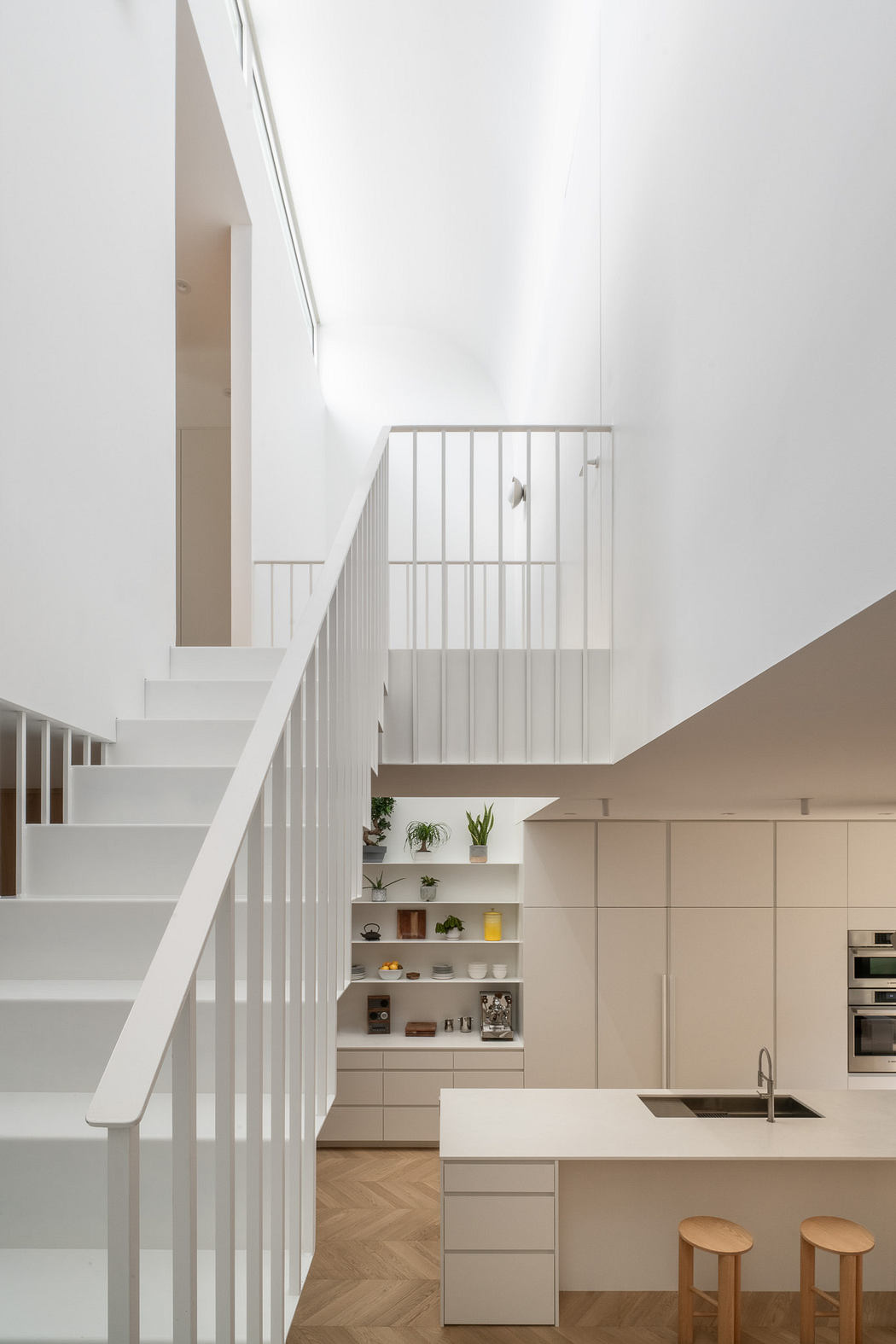 Minimalist white kitchen interior with a staircase and natural light.