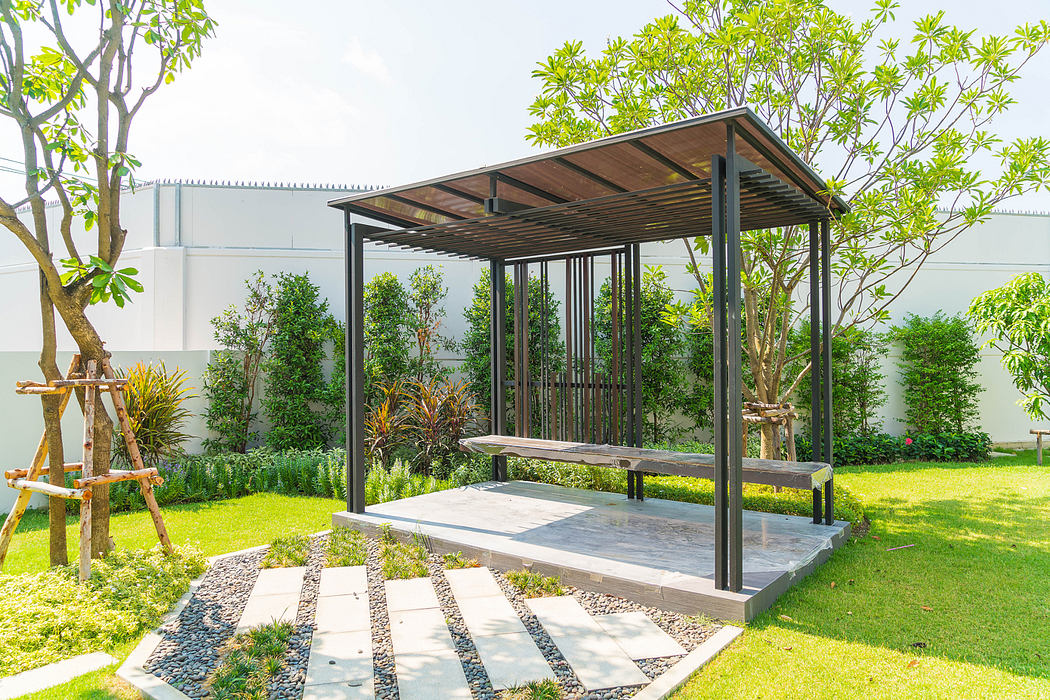 Modern outdoor gazebo with swing bench in a landscaped garden.