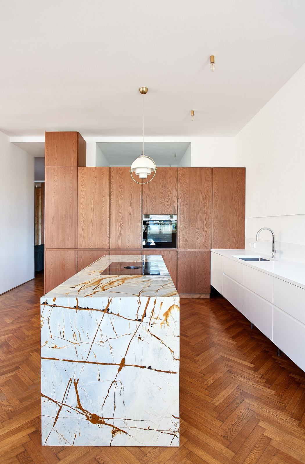 Modern kitchen with wooden cabinets and marble island on herringbone floor.