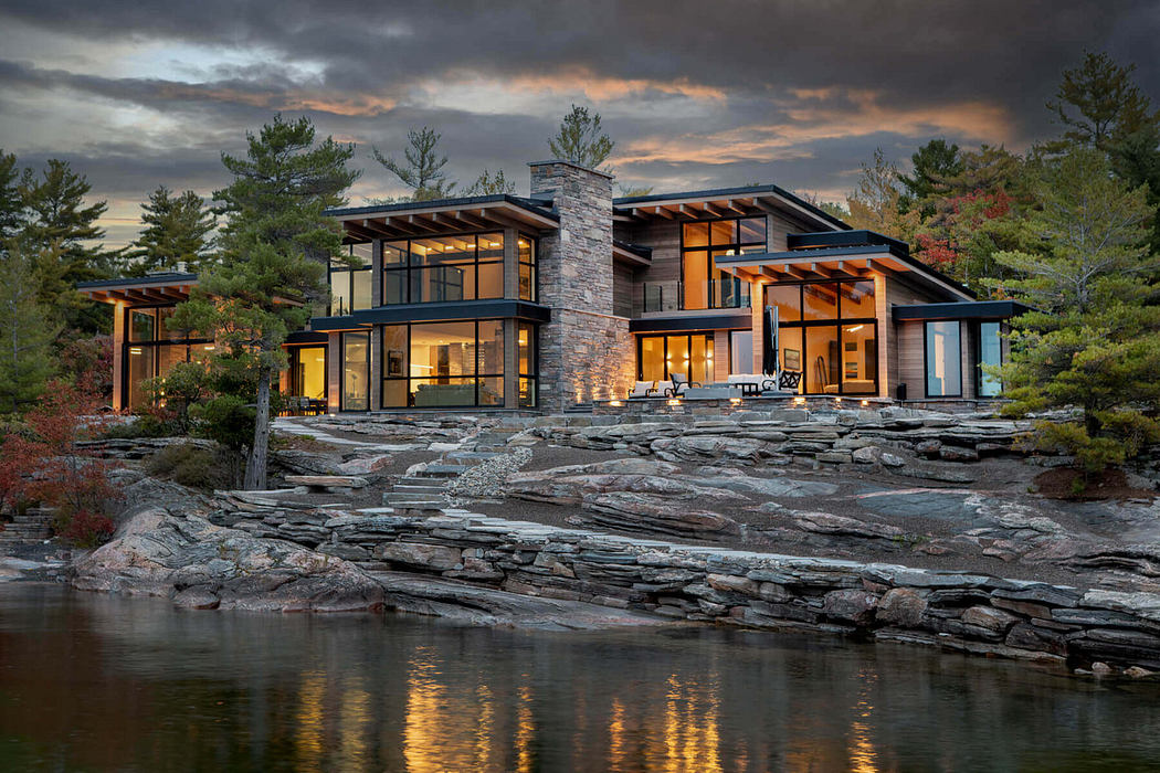 Contemporary lakeside house with expansive windows and stone details at dusk.