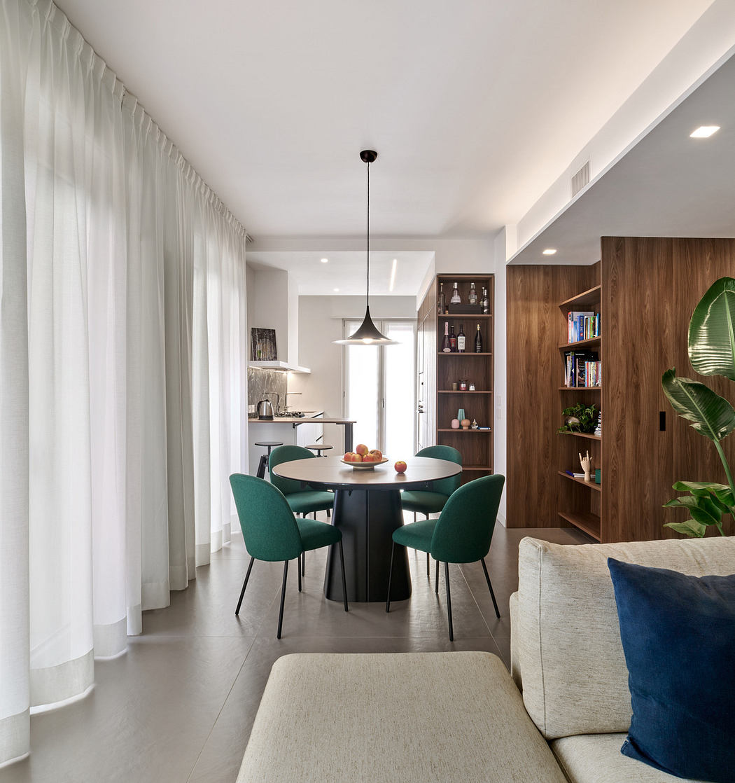 Contemporary dining area with emerald chairs, pendant light, and wooden bookshelf