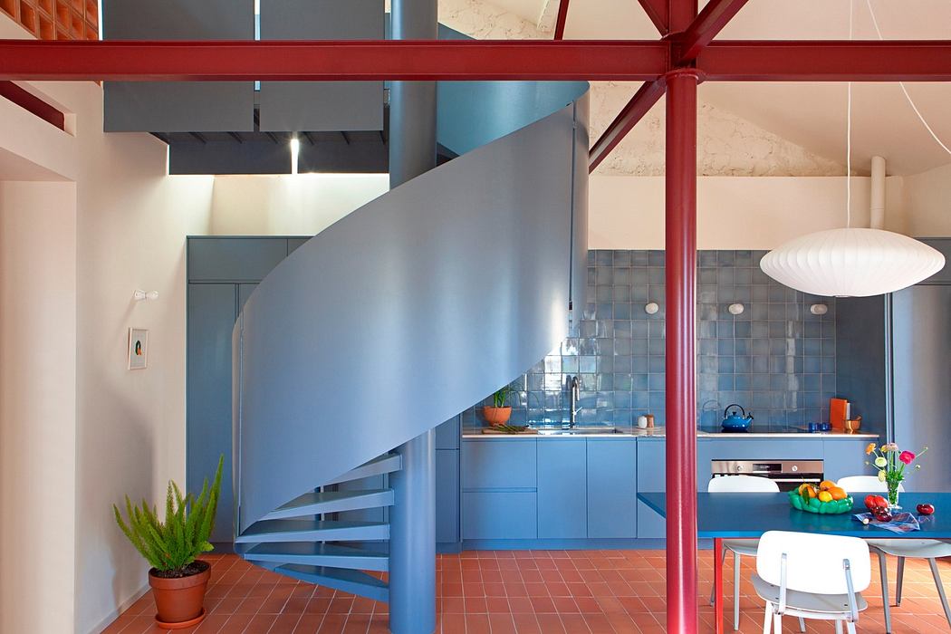 Modern interior with blue spiral staircase, red beams, and a kitchen area.