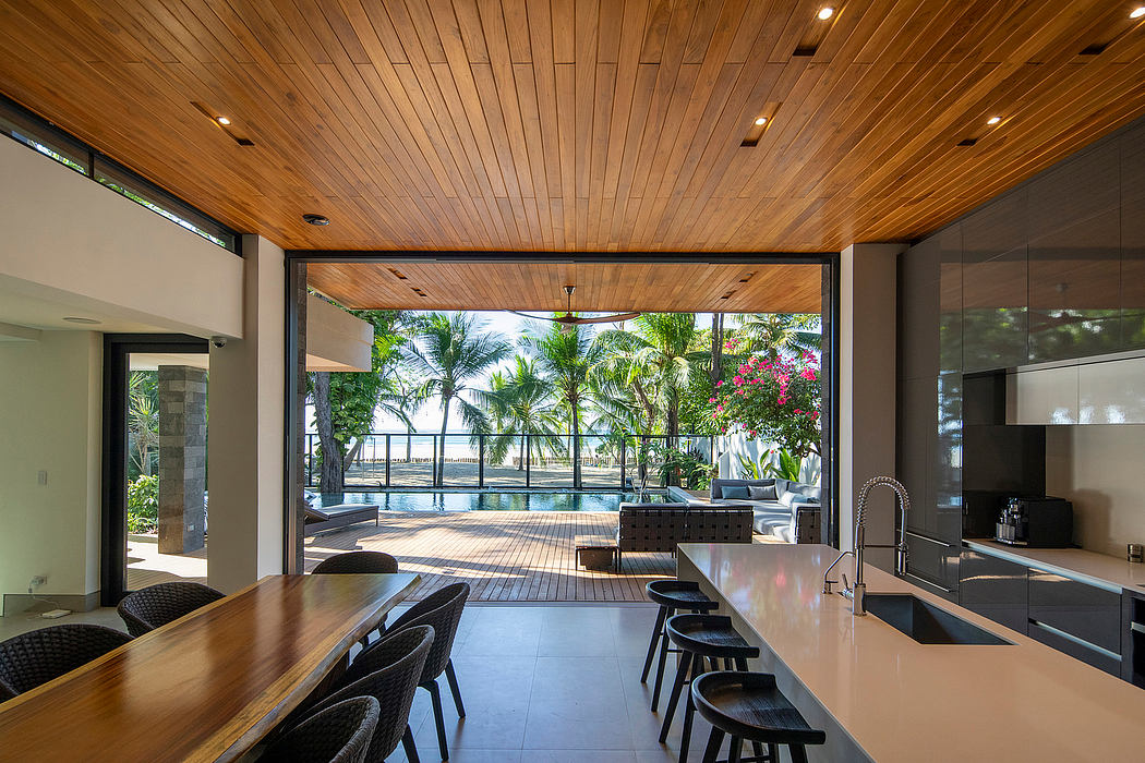Modern kitchen with wooden ceiling opening to a patio with tropical view.
