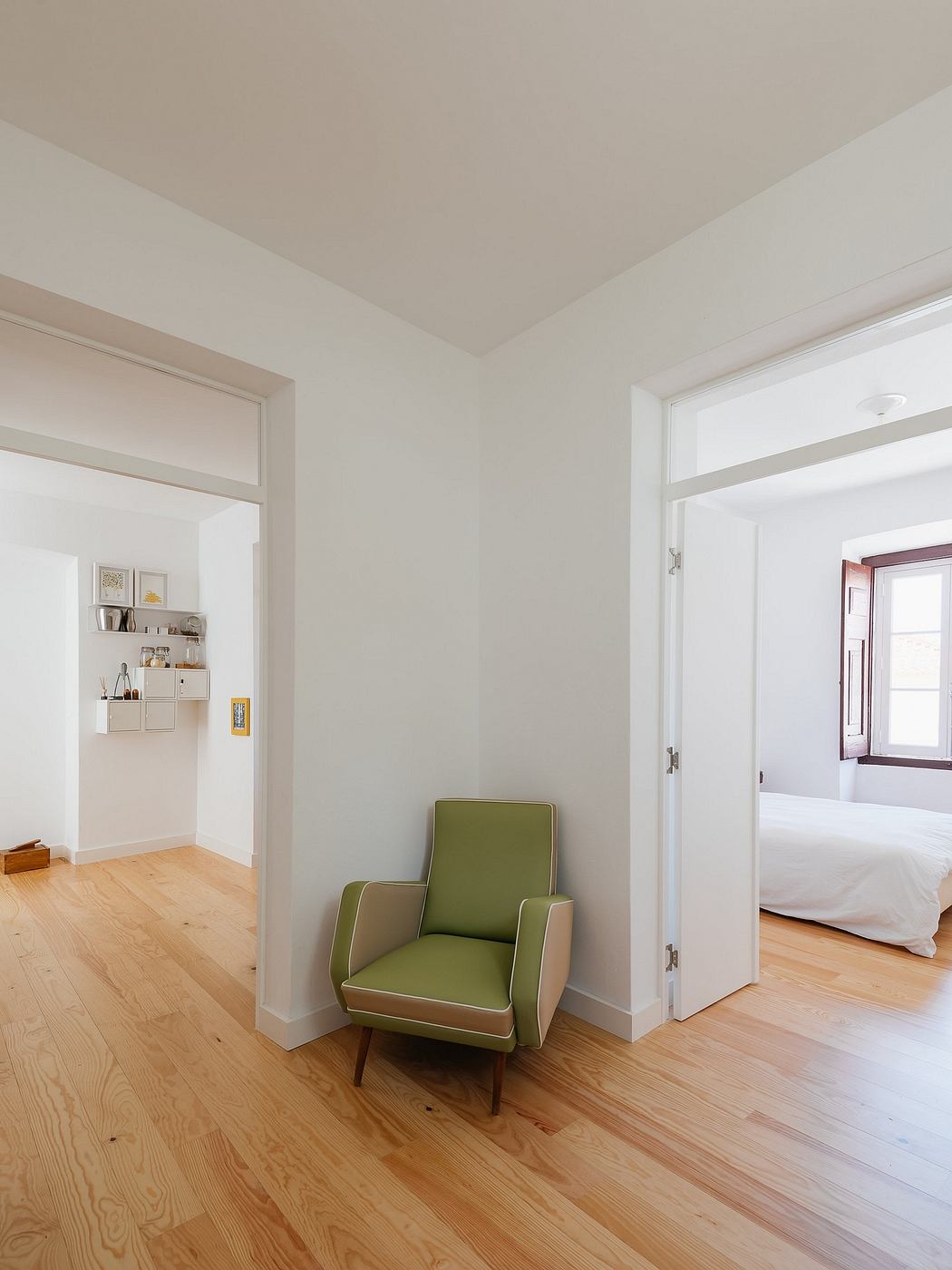 Bright, minimalistic room with a green chair, wooden floors, and open doors