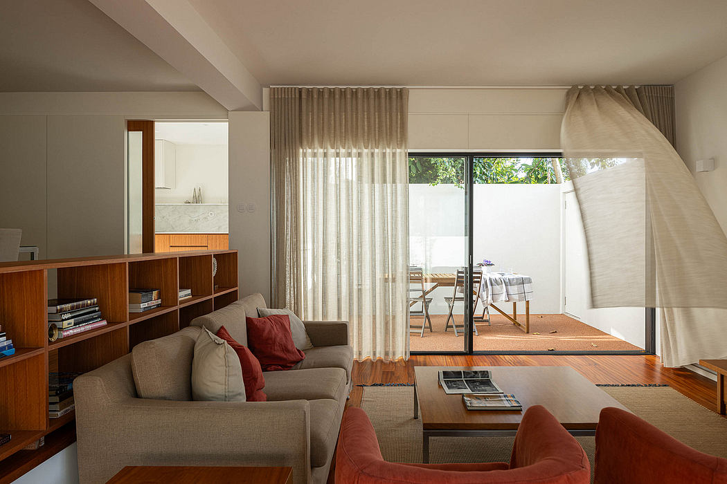 Modern living room with sofas, a wooden bookshelf, and sheer curtains.