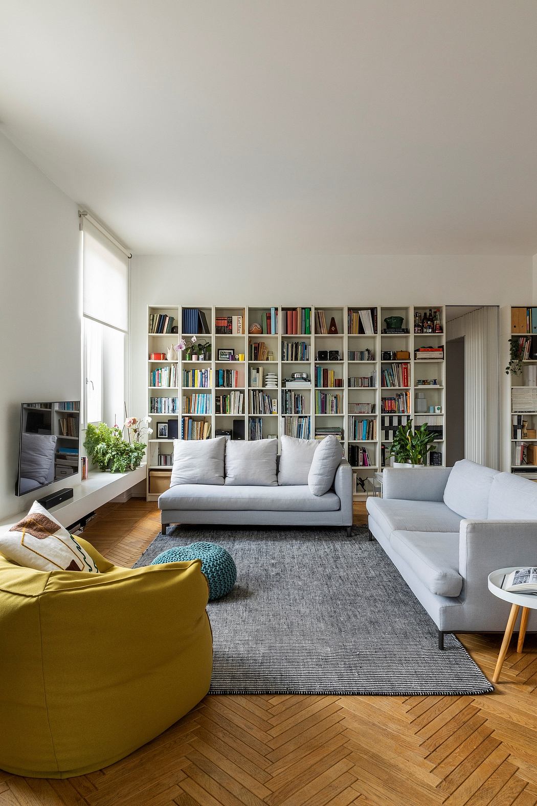 Bright living room with a full bookshelf, sofa set, and herringbone