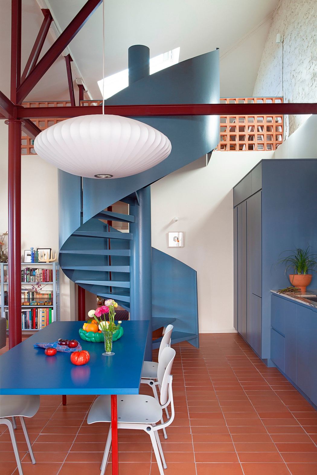 Modern interior with blue spiral staircase, terracotta floor tiles, and red structural