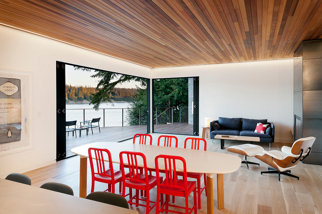 Modern lake house interior with red chairs, wooden ceiling, and large open sliding door