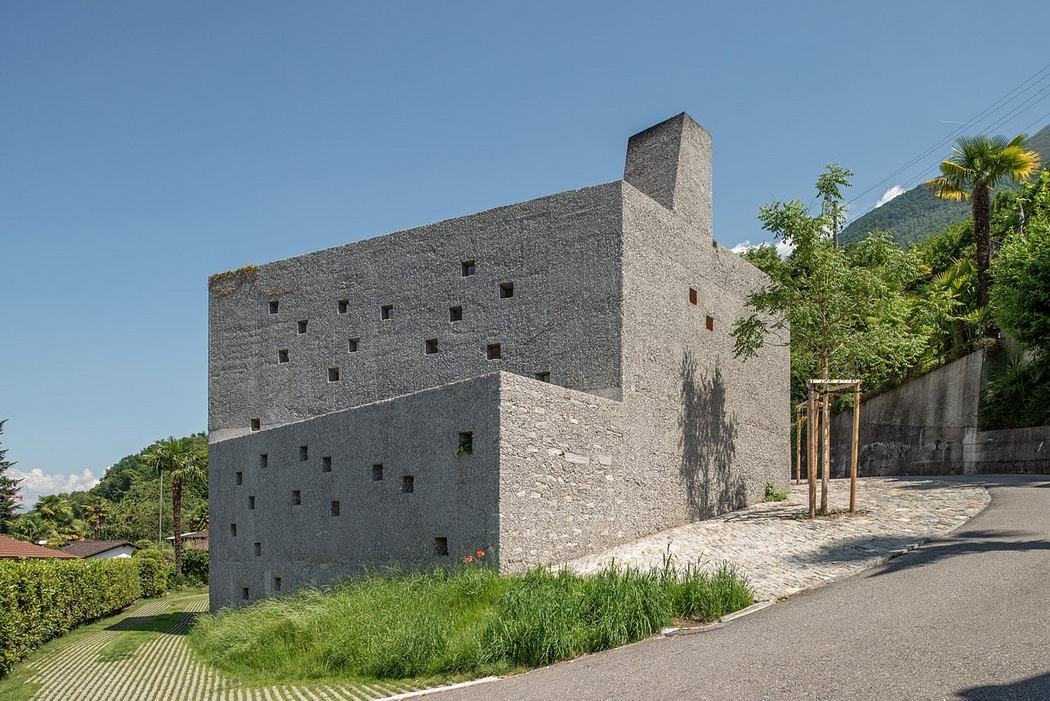 Contemporary stone building with scattered windows, set against a mountainous backdrop.