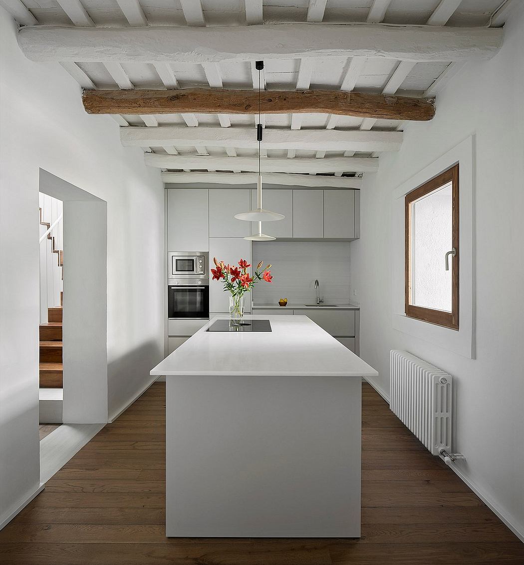 Modern kitchen interior with white cabinets, wooden floors, and exposed beams.