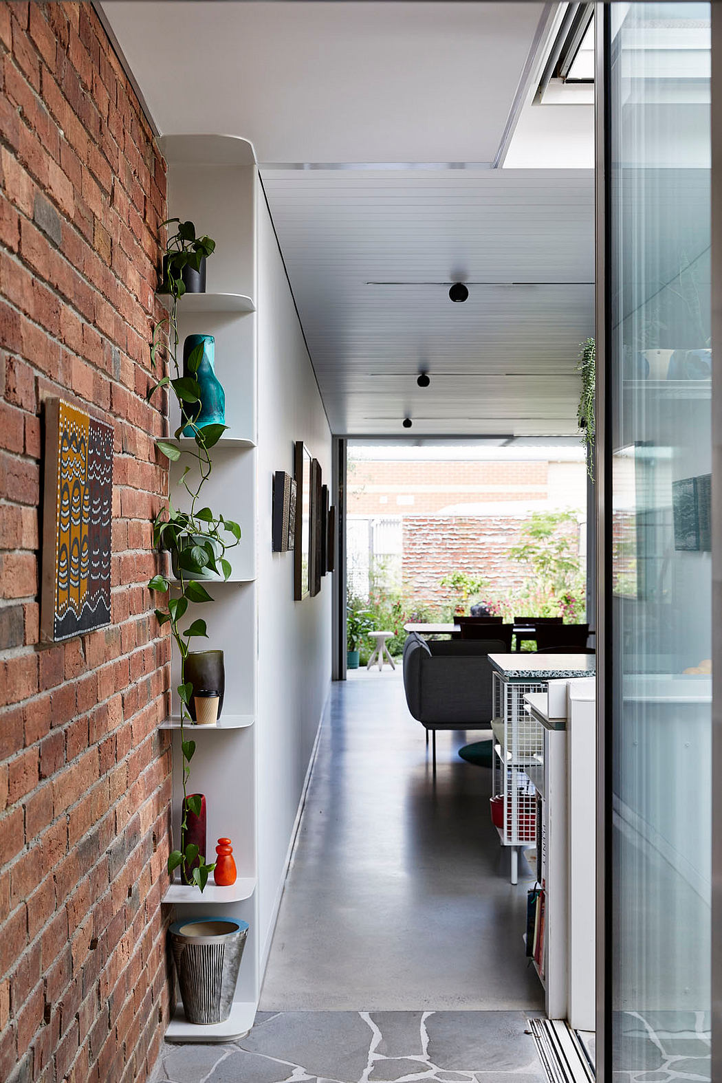 Narrow hallway with brick wall, shelves, and glass doors leading to a room