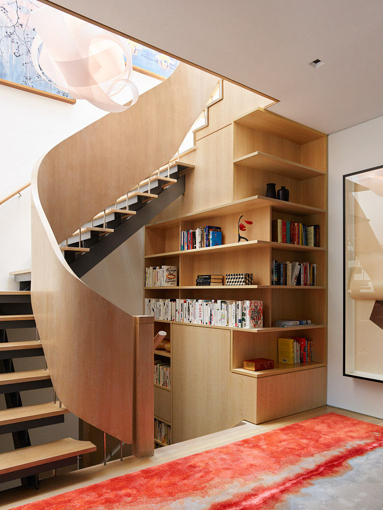 Wooden spiral staircase with integrated bookshelves in a modern room.