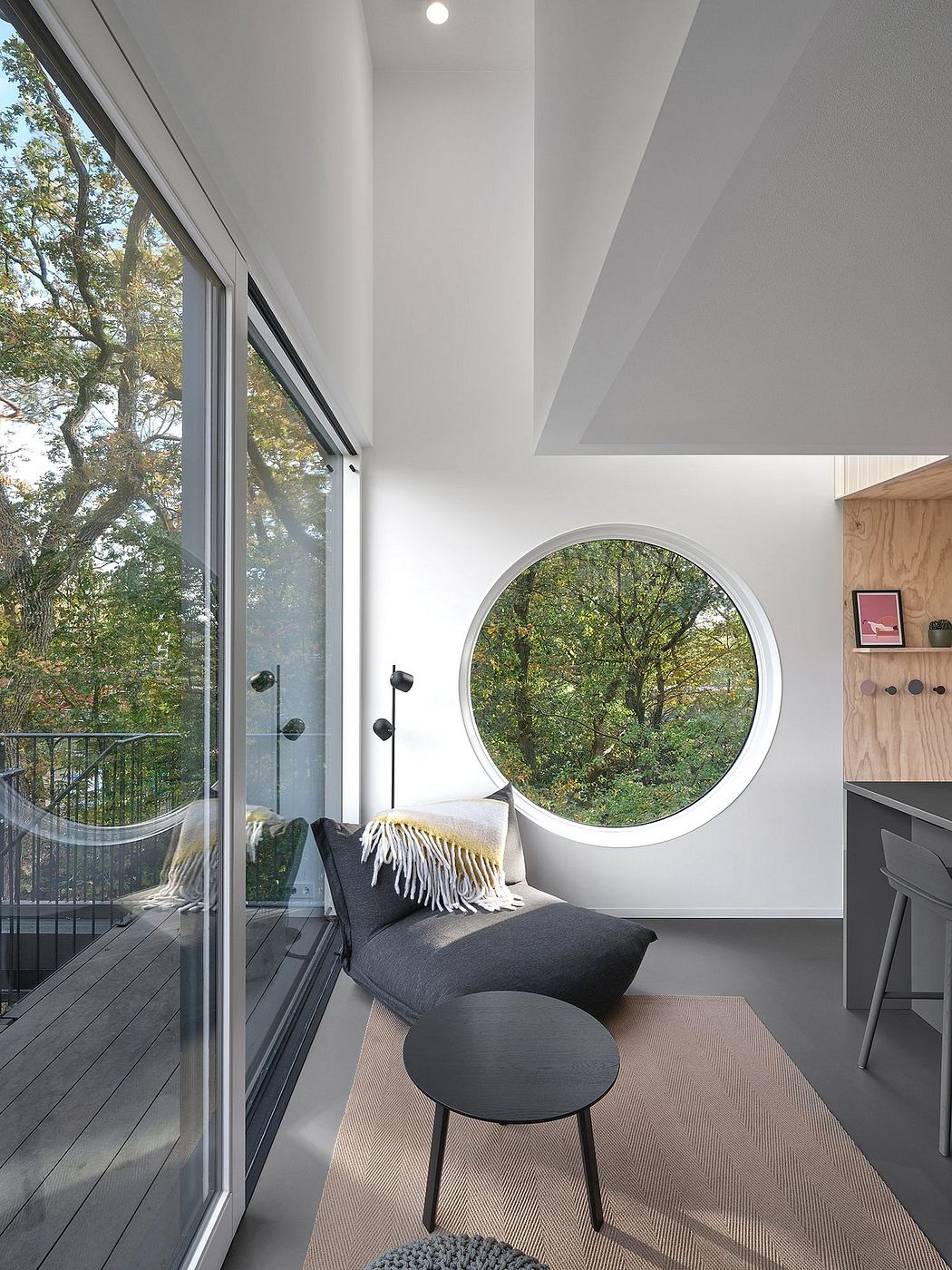 Minimalist room with circular window overlooking trees.