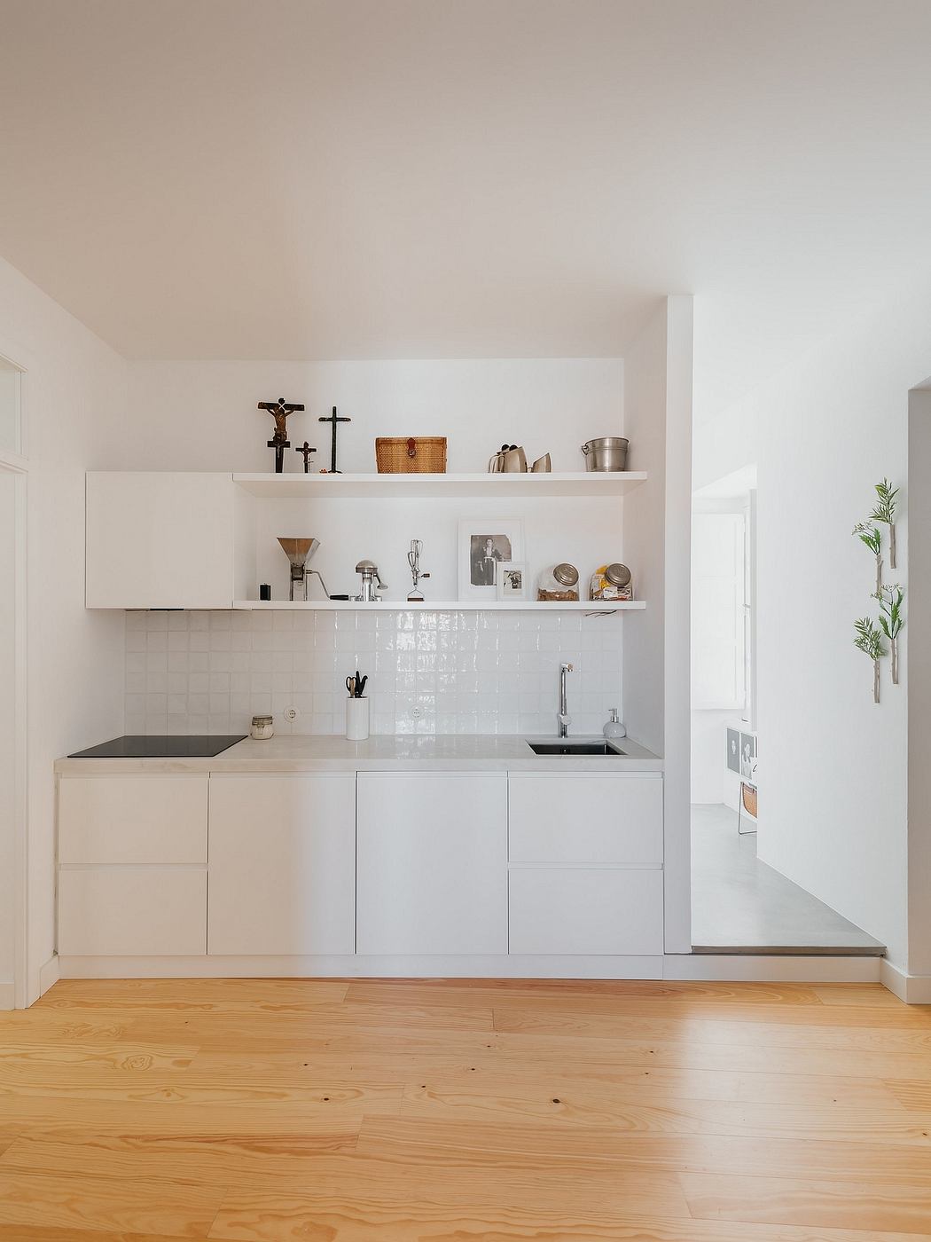 Modern, minimalist kitchen corner with white cabinetry and wooden floor.