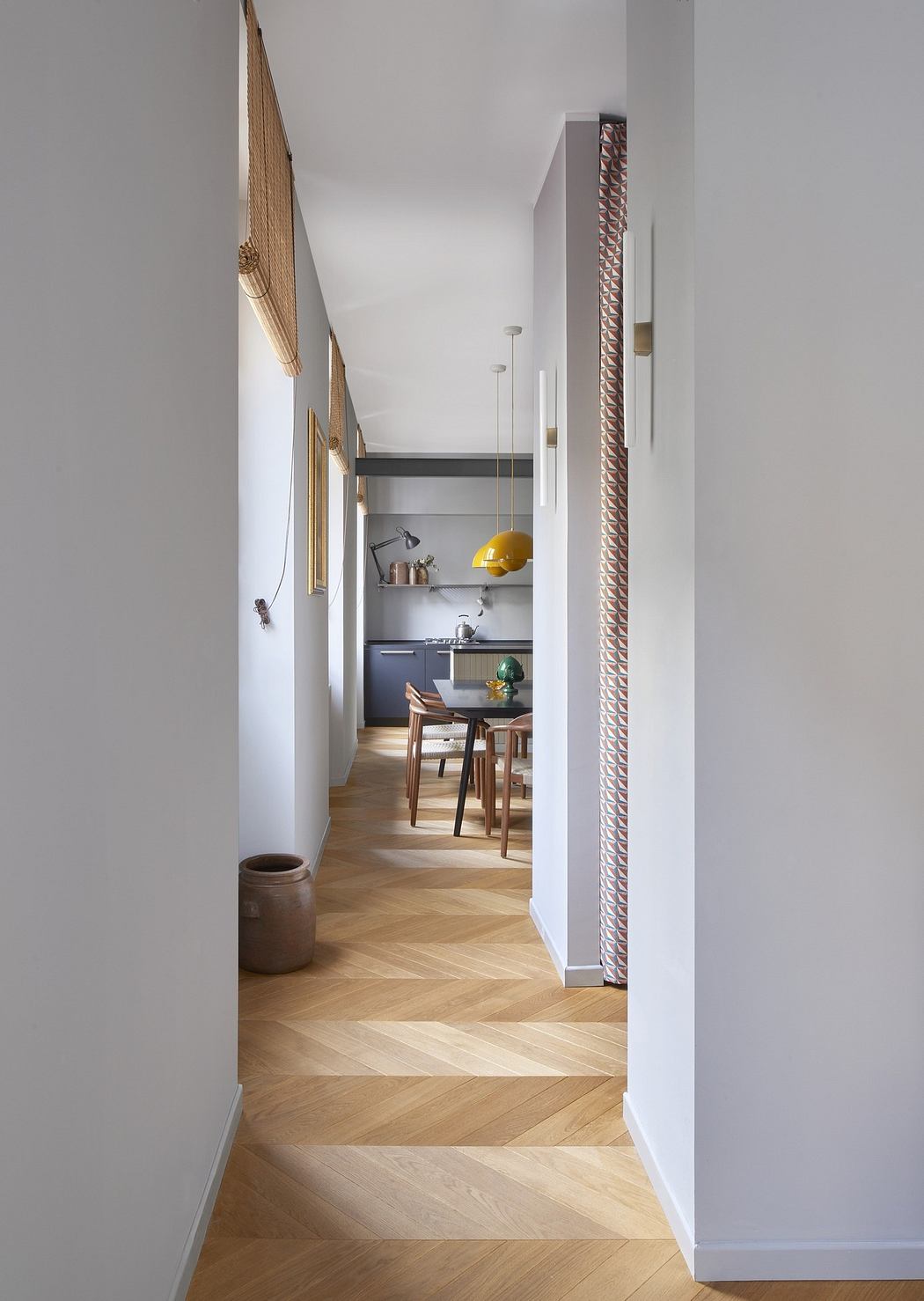Narrow hallway with herringbone wood floor leading to a kitchen.