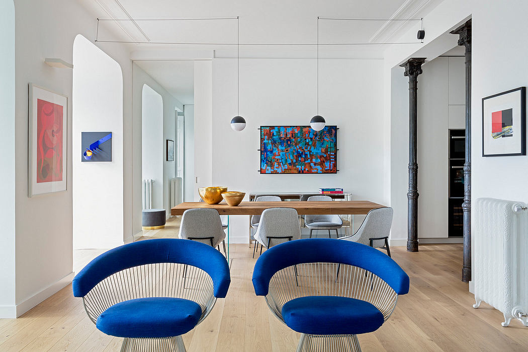 Modern dining room with blue chairs, wooden table, and colorful artwork.