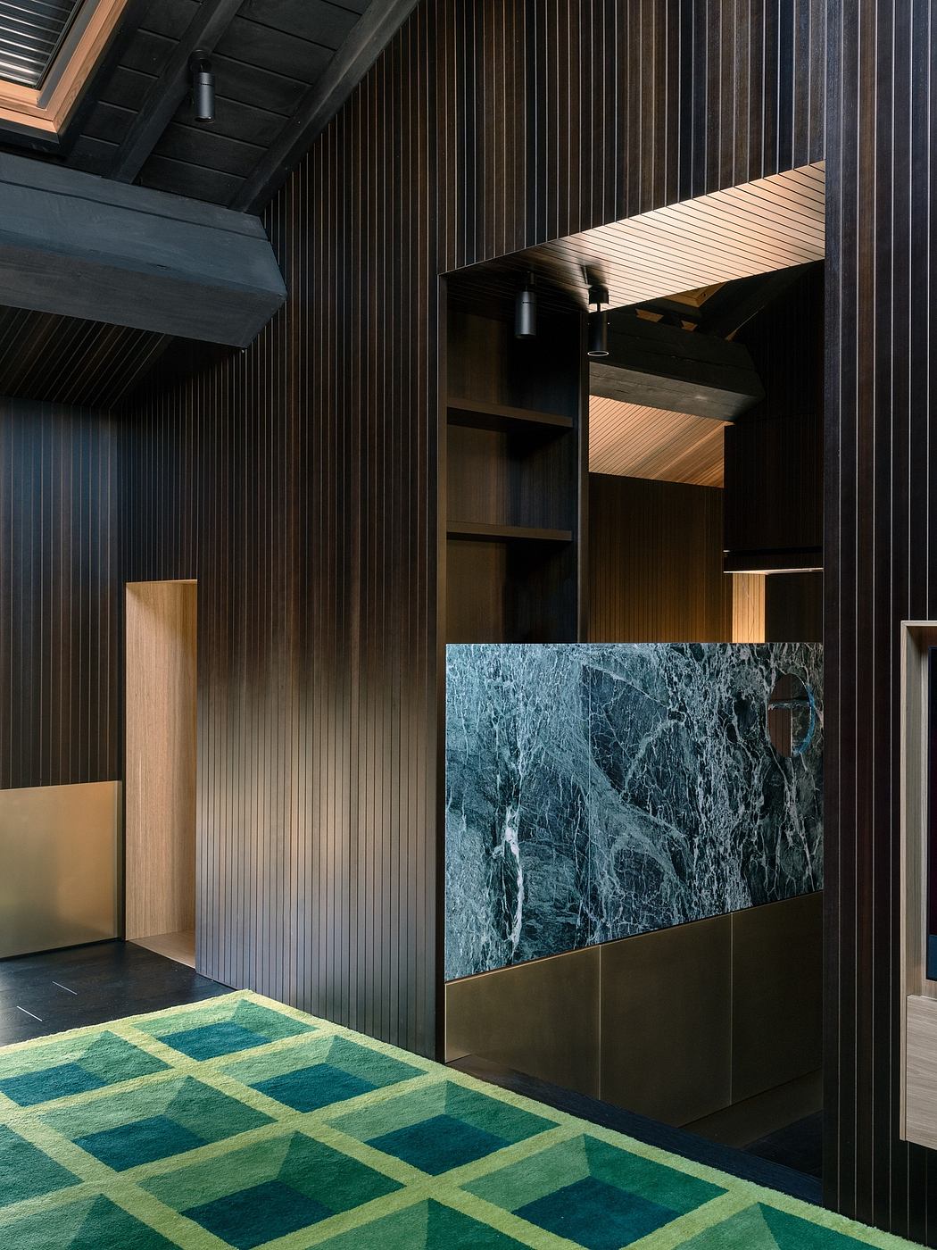 Contemporary interior with dark wood panels, marble feature, and geometric green carpet.