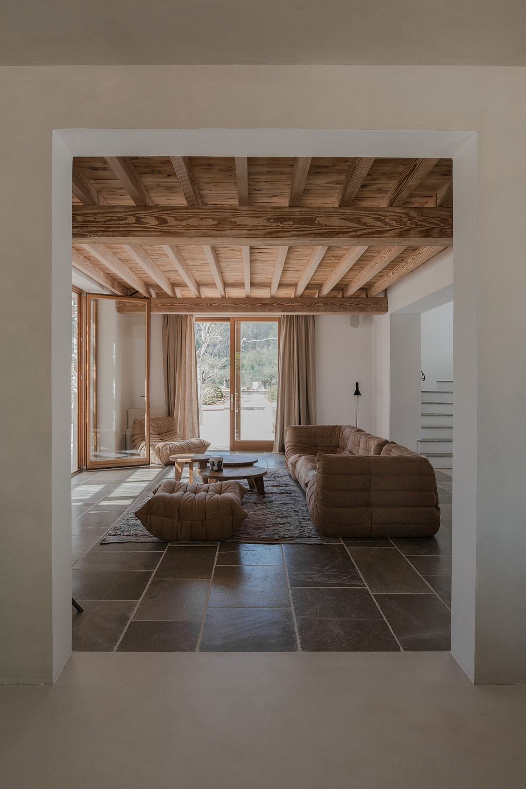 Modern room with wooden ceiling beams, plush sofas, and tile flooring.