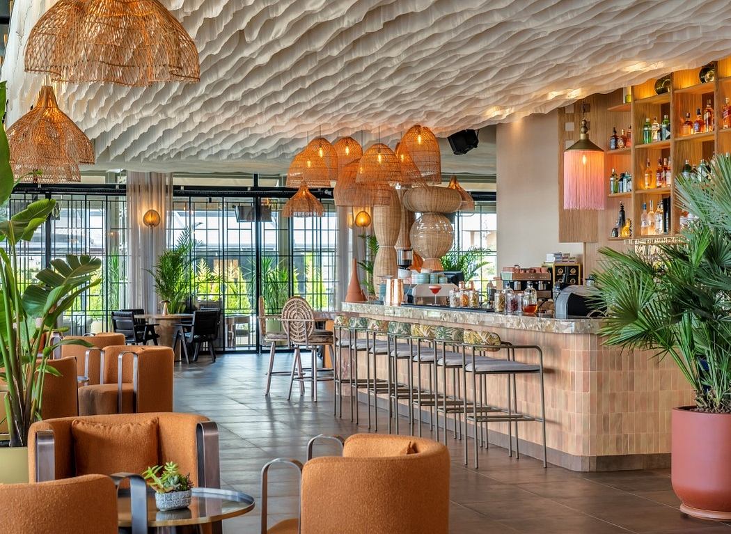 Modern cafe interior with wavy ceiling design and hanging wicker lamps.