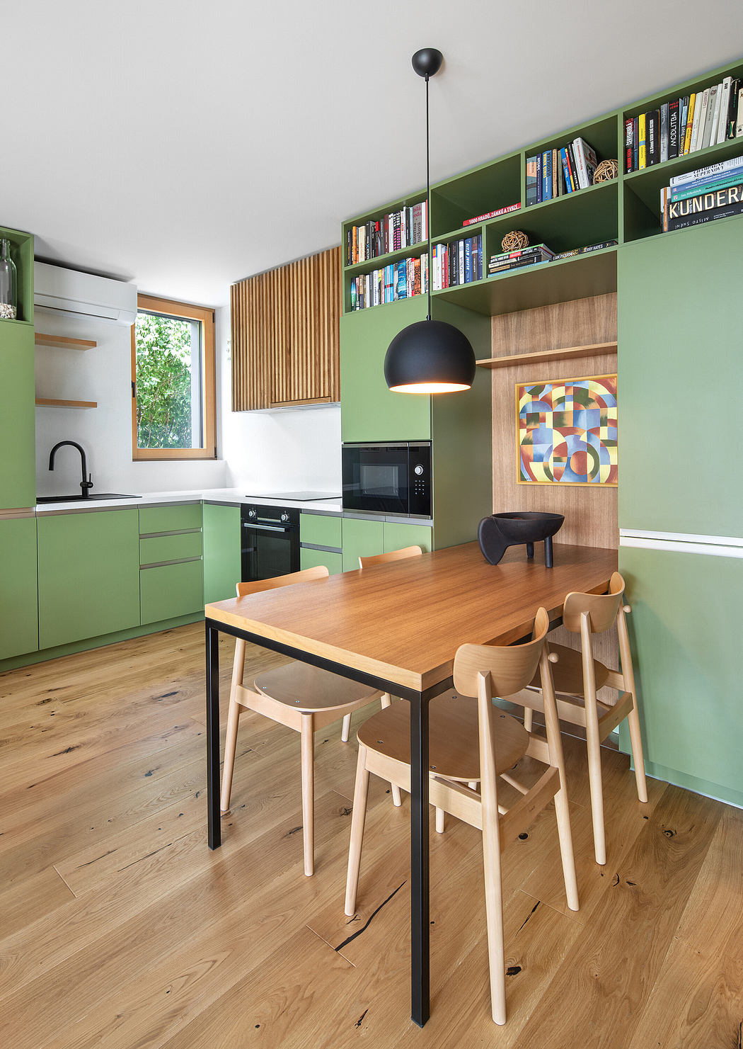 Modern kitchen with green cabinets, wooden table, chairs, and pendant light.