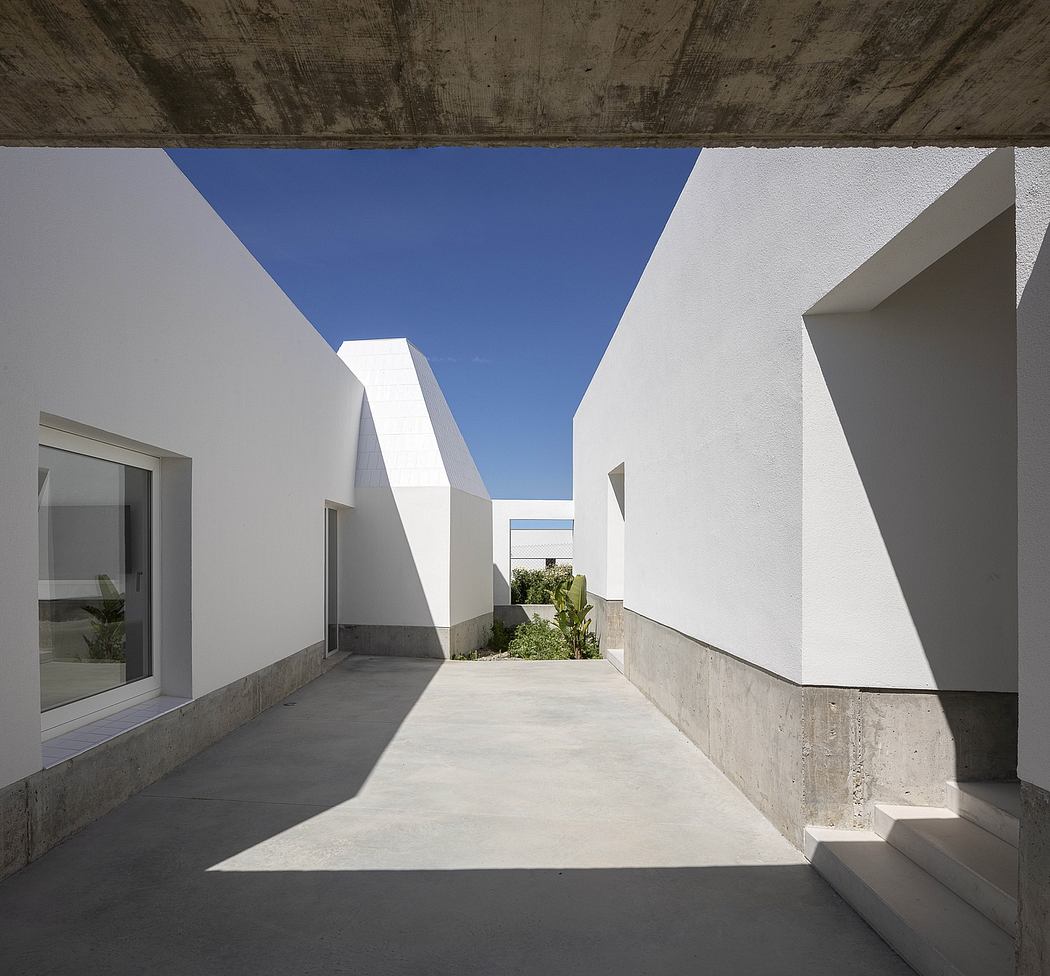 Modern courtyard with angular white walls and a clear blue sky above.