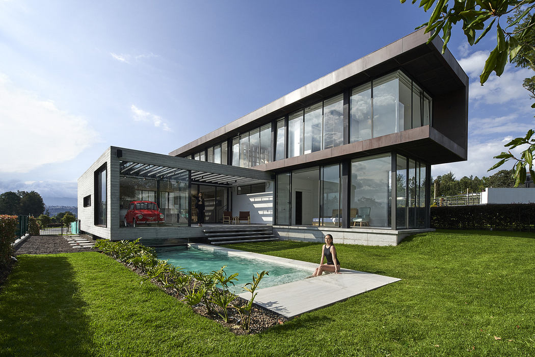 Modern house with large windows, a pool, and a person sitting nearby.