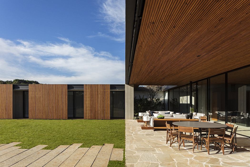 Modern house with large glass windows, wooden facade, and outdoor dining area.