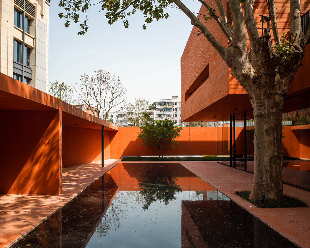 Modern orange architecture with reflective water feature and tree.