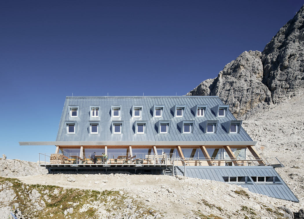 Modern mountain lodge with geometric facade against a rocky backdrop.