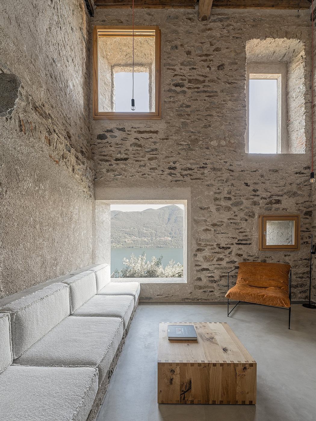 Minimalist stone room with built-in sofa, wooden chair, and scenic window view