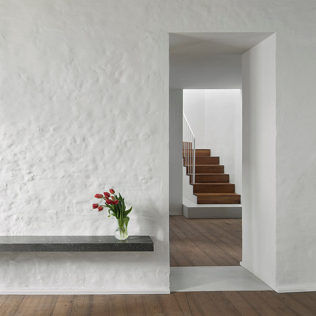 Minimalist interior with textured white walls, floating shelf, and wooden staircase.