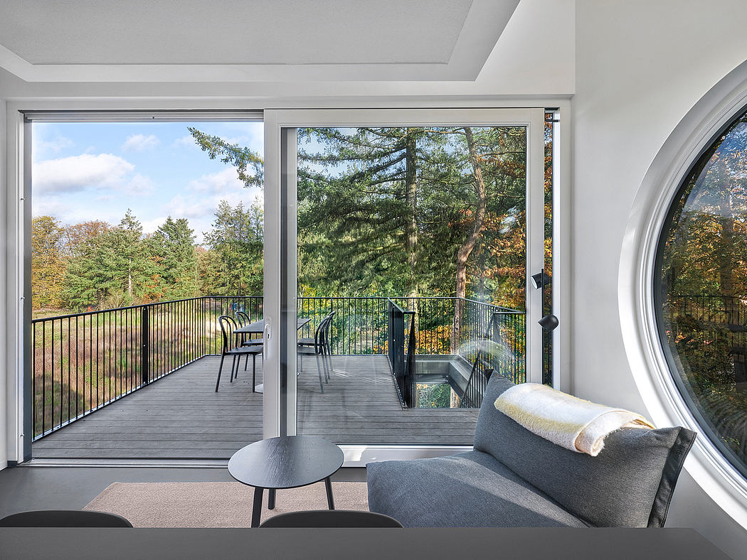 Modern room with sofa, round window, and open sliding door to balcony with trees