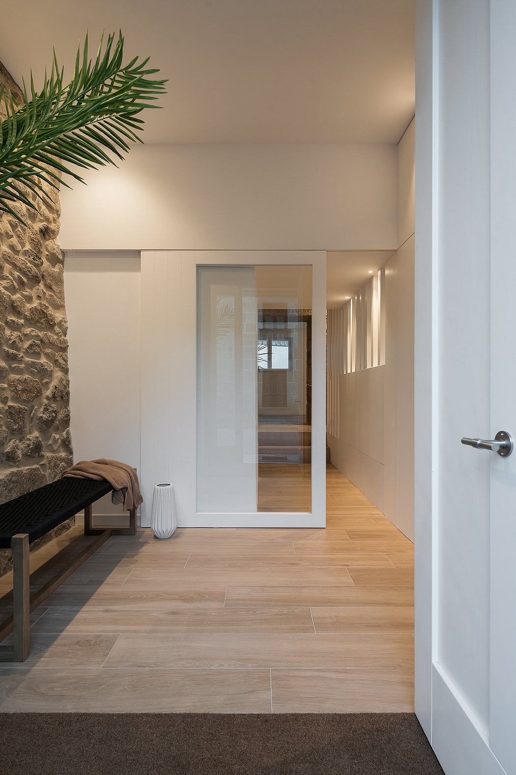 Modern hallway with stone accent wall, wooden floor, and glass door.
