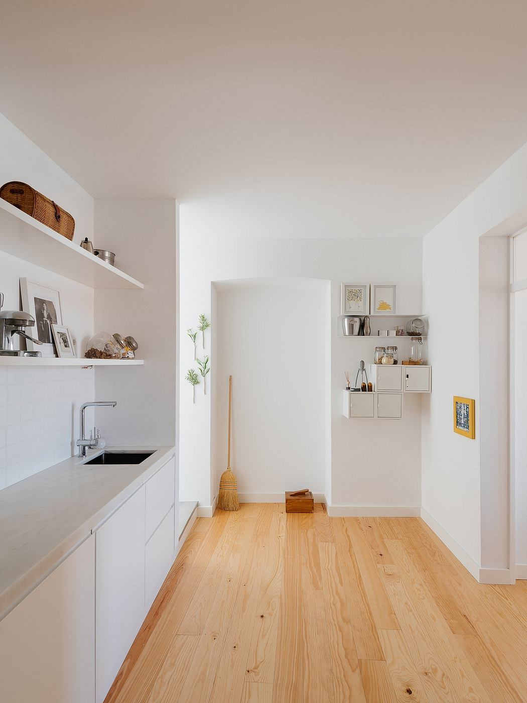 Minimalist kitchen with white cabinets, wooden floor, and open shelving.