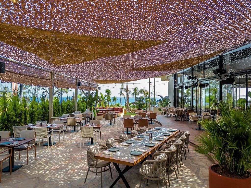 Elegant outdoor dining space with a copper-toned woven ceiling and tropical plants.
